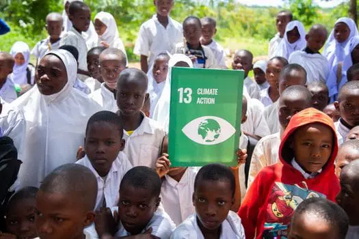 Group of students holding a Climate Action sign in outdoor environmental setting.