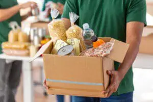 A volunteer holds a box of food while other volunteers pack more food behind.