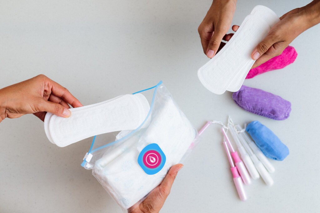 Two people distributing packs of menstrual products (pads and tampons). One of the packs has the EmpowerHer Flow logo on it.