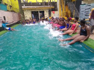 Swimming camp participants practicing their kicking in the pool with the help of camp coach Mr. Paul Yoga.