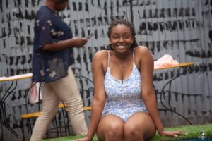 A female swimming camp participant smiling at the camera while sitting by the pool.