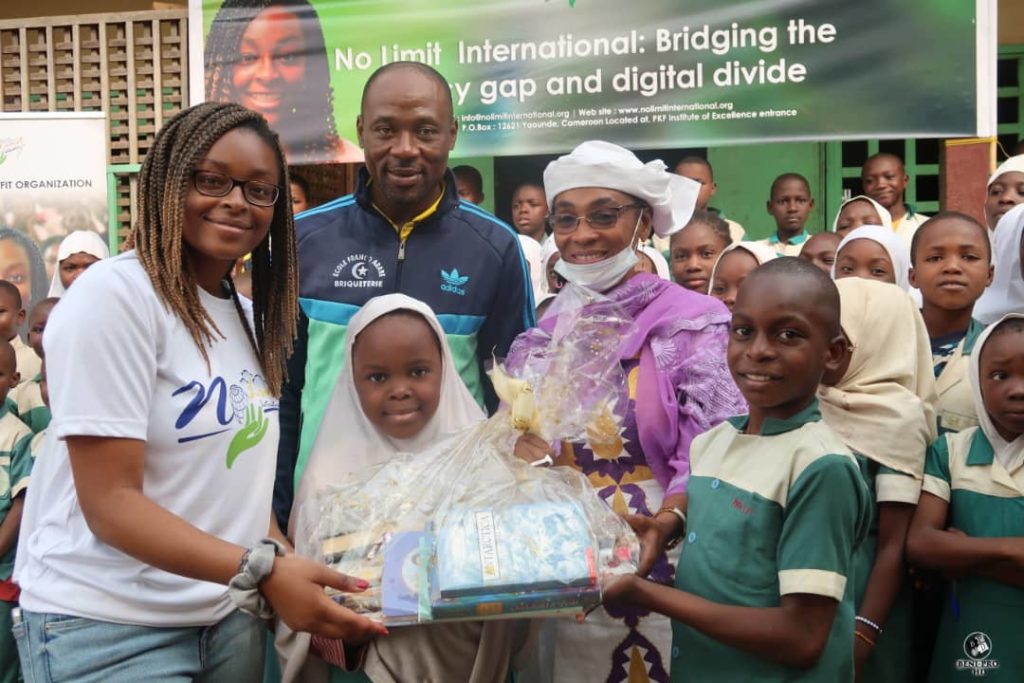 No Limit International Co-Founder Orlyanka Tantchou stands with students and faculty of the Franco-Arab primary school with a bag of children's books. The principal of the school, Ms. Aminata Ahidjo, received the donation of books, tablets, and laptops to the primary school.