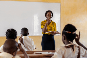 A female teacher in Africa teaches to a group of schoolchildren.