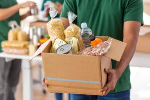 A volunteer holds a box of food while other volunteers pack more food behind.