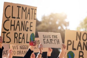 A group of climate activists holding up signs that advocate for environmental change. Example signs read: “Climate change is real,” “Save the Earth,” and “No plan B.”