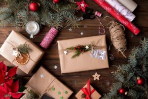 Image description: A layout of Christmas items and decorations, including pine trees with ornaments, poinsettias, dried oranges, and presents wrapped in an-eco friendly gift wrap.